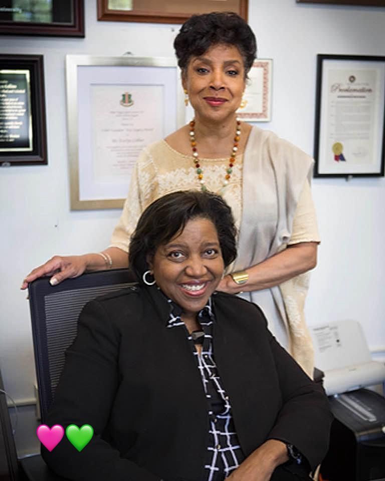 Phylicia Rashad stands behind a seated Dr. Evelyn Collins in an office hung with framed awards and proclamations.