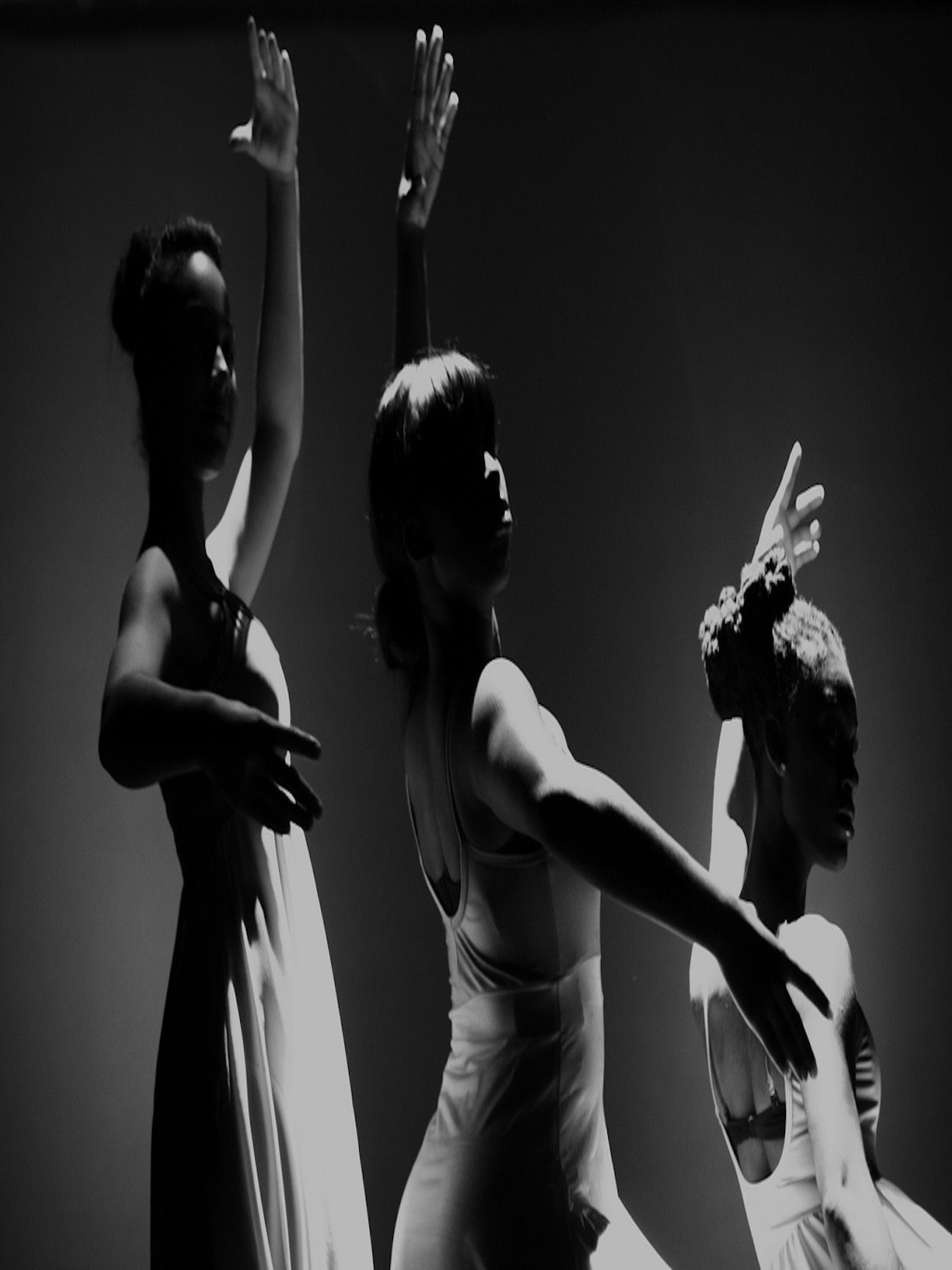 Three dancers in dramatic silhouette, arms lifted against the stage light.